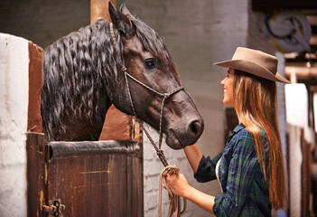 Would you like a pat. An attractive young cowgirl bonding with her horse in the stable.