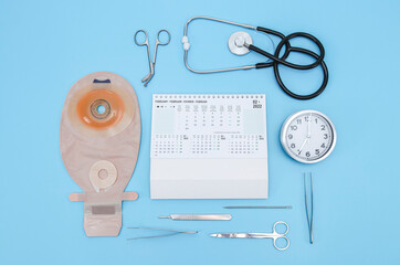 A colostomy bag, February 2022 calendar, surgical instruments, a stethoscope and a cloc on a blue .