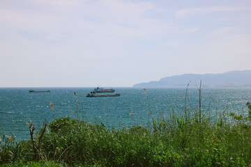 Seascape, ships, grass, and island in the distance.