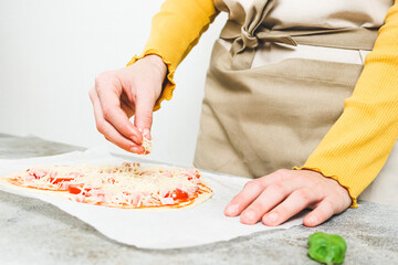 Hand of caucasian teenage girl pouring grated cheese on pizza hearts for valentine's day.