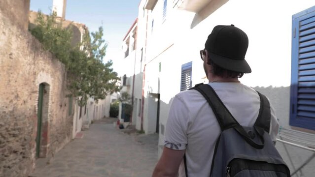 Slow mo, male traveler with baseball hat and backpack walk down European alleyway