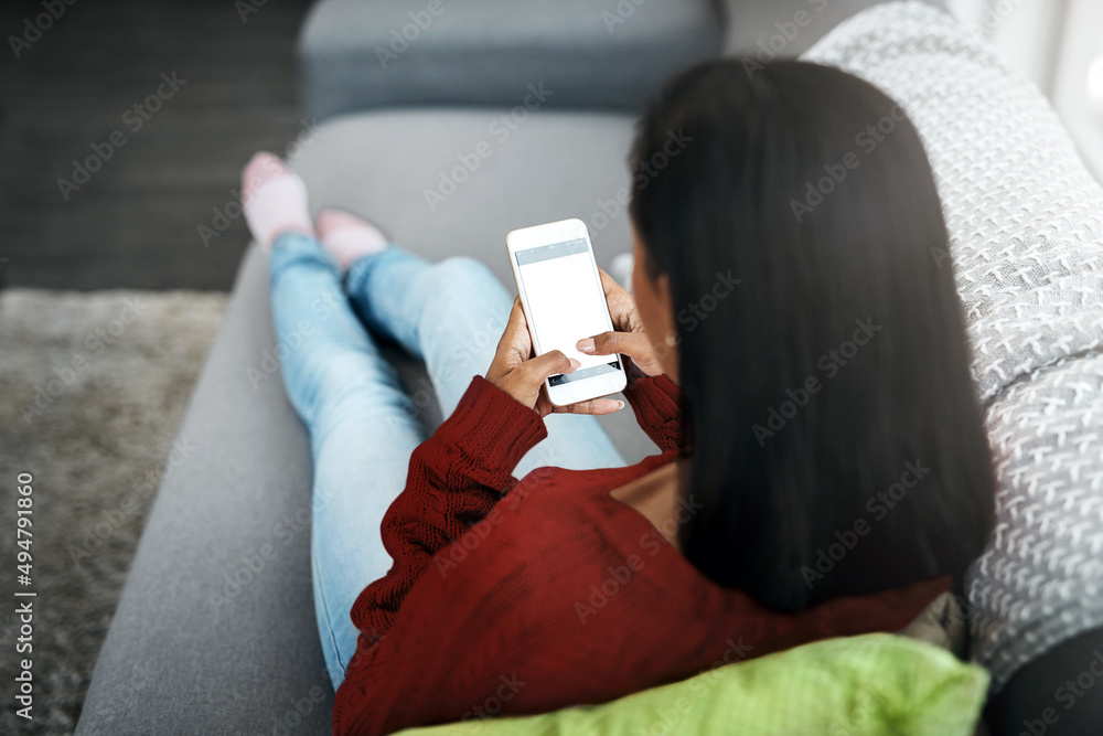 Poster What I like to do to relax. Rearview shot of an unrecognizable woman using a cellphone while chilling on the sofa in the living room at home.