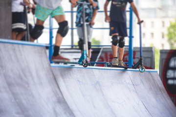 Skate park view with kids on a kick scooter doing tricks and stunts, boys in a skate park riding...