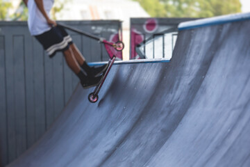 Skate park view with kids on a kick scooter doing tricks and stunts, boys in a skate park riding...