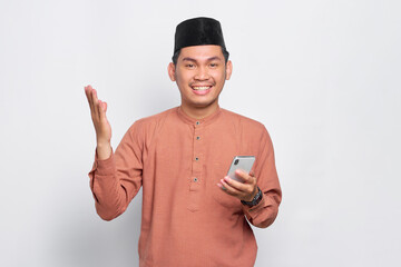 Cheerful young Asian Muslim man using a mobile phone and celebrating success, getting good news isolated over white background
