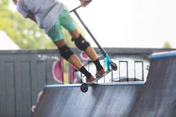 Skate park view with kids on a kick scooter doing tricks and stunts, boys in a skate park riding...
