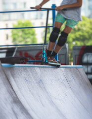 Skate park view with kids on a kick scooter doing tricks and stunts, boys in a skate park riding...