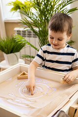 Cute baby little boy drawing smiley fun face on sand table therapy fine motor skills top view