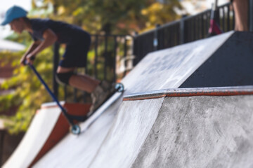 Skate park view with kids on a kick scooter doing tricks and stunts, boys in a skate park riding...