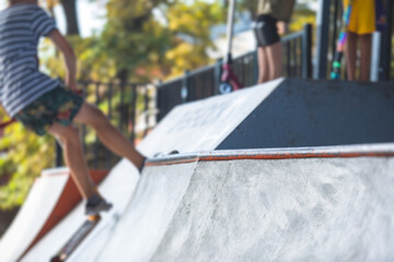 Skate park view with kids on a kick scooter doing tricks and stunts, boys in a skate park riding...