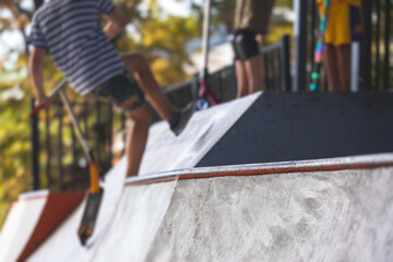 Skate park view with kids on a kick scooter doing tricks and stunts, boys in a skate park riding...