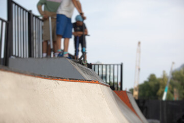 Skate park view with kids on a kick scooter doing tricks and stunts, boys in a skate park riding...