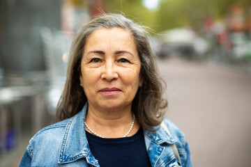 Portrait of smiling modern aged woman wearing denim jacket enjoying walk around city in spring day.