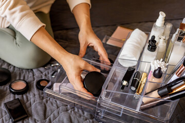 Closeup female hands putting luxury cosmetic into acrylic box with drawer storage organization