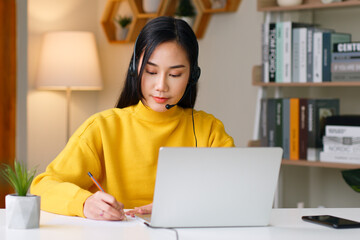 Young Asian woman wearing headphone studying online education at home via laptop