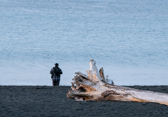 Silhouette of man fishing on the beach at sunrise with wooden log on the sand
