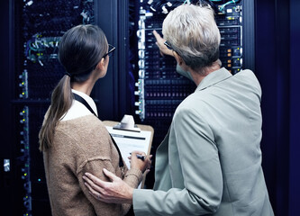 Day one in a new data centre. Rearview shot of two technicians working together in a sever room.