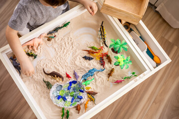 Top view cute little baby boy playing sensory box dinosaur world with kinetic sand table