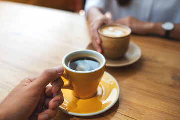 Closeup image of a young couple holding and drinking coffee together in cafe