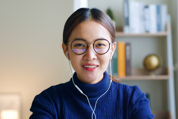 Young Asian woman creator wearing glasses and headphone talking on video call conference or virtual...