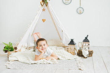 Little caucasian boy laughing while lying in a toy kids teepee in a white scandinavian christmas interior. © July P