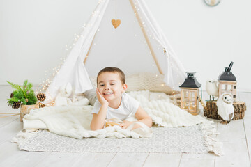 Little caucasian boy laughing while lying in a toy kids teepee in a white scandinavian christmas interior. © July P