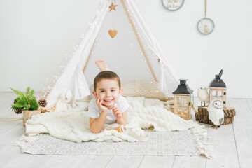 Little caucasian boy laughing while lying in a toy kids teepee in a white scandinavian christmas...
