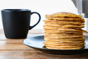 Stack of pancakes, dark mug and coffee pot on wooden table Close-up