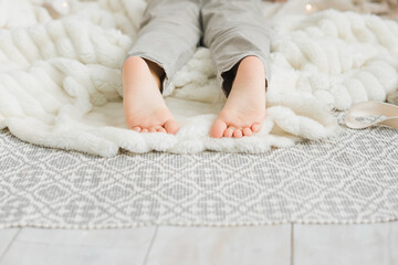 Feet of a little caucasian boy on a white plaid close-up with copy space.