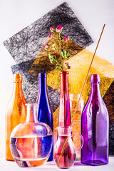 Still life with colored glassware and rose branch on an abstract background