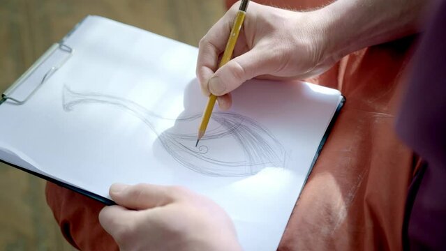The artist drawing a flat line with a black pencil. Artists hands drawing wooden pencil writes line on paper.