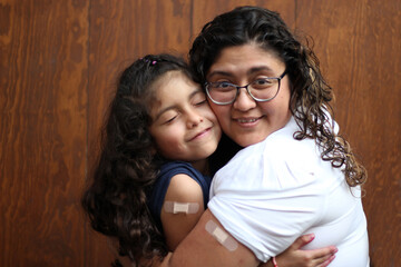 Happy and hugging Latin mom and daughter show their recently vaccinated arms against Covid-19 in the new normality due to the Coronavirus pandemic
