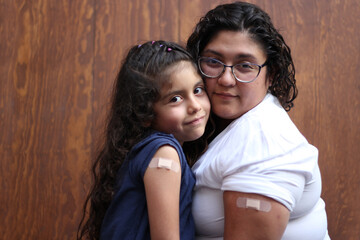 Happy and hugging Latin mom and daughter show their recently vaccinated arms against Covid-19 in the new normality due to the Coronavirus pandemic
