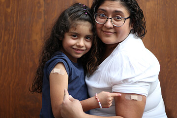 Happy and hugging Latin mom and daughter show their recently vaccinated arms against Covid-19 in...