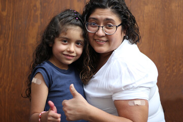 Happy and hugging Latin mom and daughter show their recently vaccinated arms against Covid-19 in the new normality due to the Coronavirus pandemic
