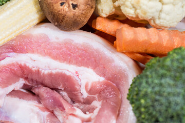 Close up piece fresh raw meat of pork belly and many vegetables are baby corn, broccoli flowers, mushroom, carrot, cauliflower Ingredients for food preparation cooking