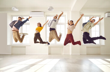 Members of a contemporary choreography dance crew jumping high up in the air all together. Group of happy, cheerful, excited, agile, energetic young people having fun in a bright hall room interior