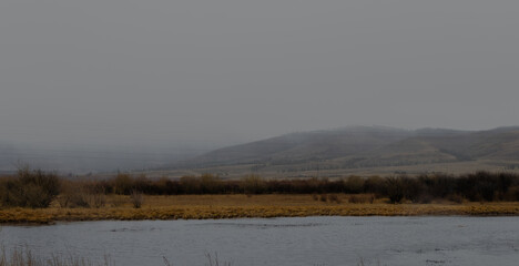 View of the river in cloudy rainy weather. Hills in the fog.