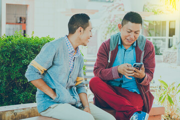 man showing his cell phone to another guy, two guys checking their cell phones, Two young men comparing their cell phones
