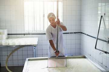 Shes making cheese. Cropped shot of a young female farm worker making cheese in a factory on the...