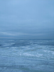 A frozen icy river and a cloudy sky in a single color connected on the horizon line.