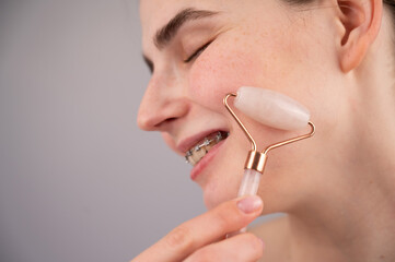 Close-up portrait of a woman uses a quartz roller massager to smooth wrinkles on her forehead.