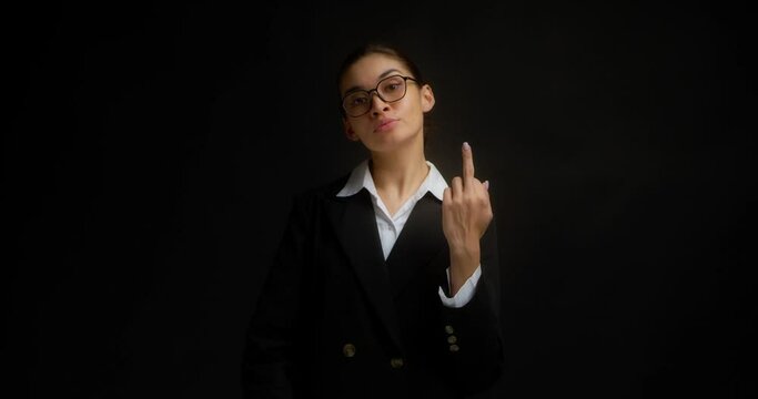 Confident, serious business woman in glasses and office clothes shows the middle finger, fuck you, fuck off, with a haughty face. Isolated on a black background in the studio