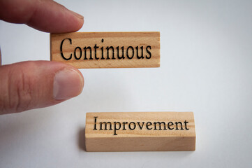 Continuous improvement text on wooden blocks. Hand holding and white background.