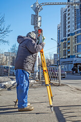 A man works with a geodesic device on a city street on a sunny day