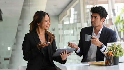A businessman is sipping coffee while talking with a female colleague