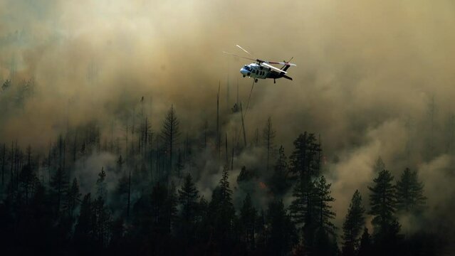 Extinguisher helicopter flying over smoking, hazy wildfire forest, in West USA