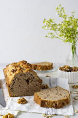 Homemade bread with seeds and nuts on a light table. A transparent vase with flowers and a bowl of nuts in the background. Slices of sliced bread on the table. Light background, space for text
