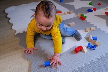 happy baby playing on play mat with wooden blocks at home. 9 months