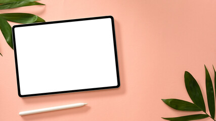 Digital tablet touchpad with stylus pen and palm leaves on pink background.